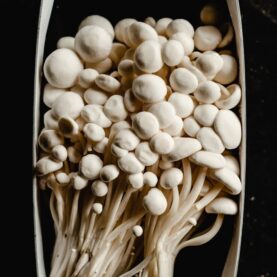 A close-up of fresh enoki mushrooms arranged in a packaging box, highlighting their unique texture.